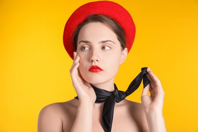 Photo of Beautiful young woman with red beret and black neckerchief on yellow background