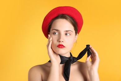 Photo of Beautiful young woman with red beret and black neckerchief on yellow background