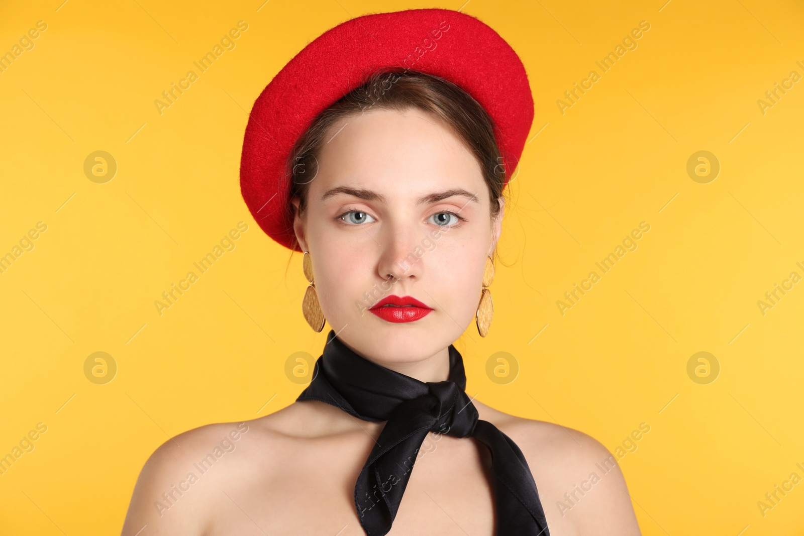 Photo of Beautiful young woman with red beret and black neckerchief on yellow background