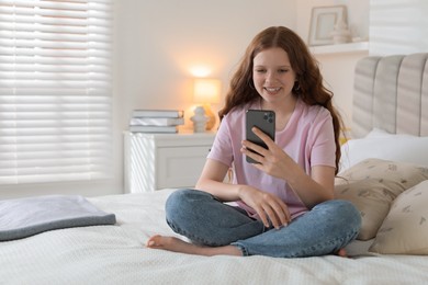 Photo of Beautiful teenage girl using smartphone on bed at home, space for text