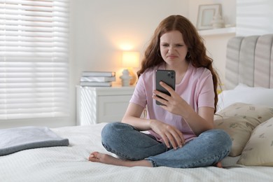 Photo of Emotional teenage girl using smartphone on bed at home, space for text