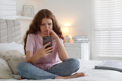 Photo of Emotional teenage girl using smartphone on bed at home, space for text