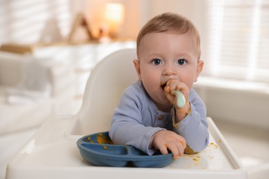 Photo of Cute little baby eating healthy food in high chair indoors