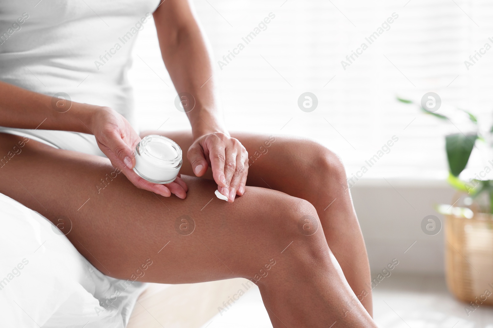 Photo of Woman applying cream onto leg at home, closeup