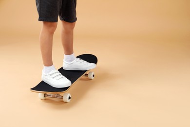 Photo of Little boy with skateboard on beige background, closeup. Space for text