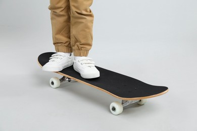 Photo of Little boy with skateboard on light grey background, closeup