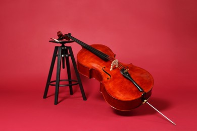 Photo of Beautiful cello and stool on red background. Classic musical instrument