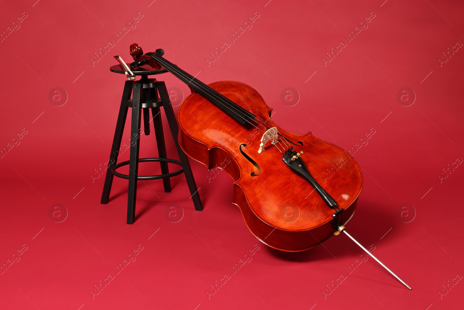 Photo of Beautiful cello and stool on red background. Classic musical instrument