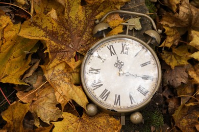 Photo of Autumn time. Vintage clock on fallen leaves in park, closeup