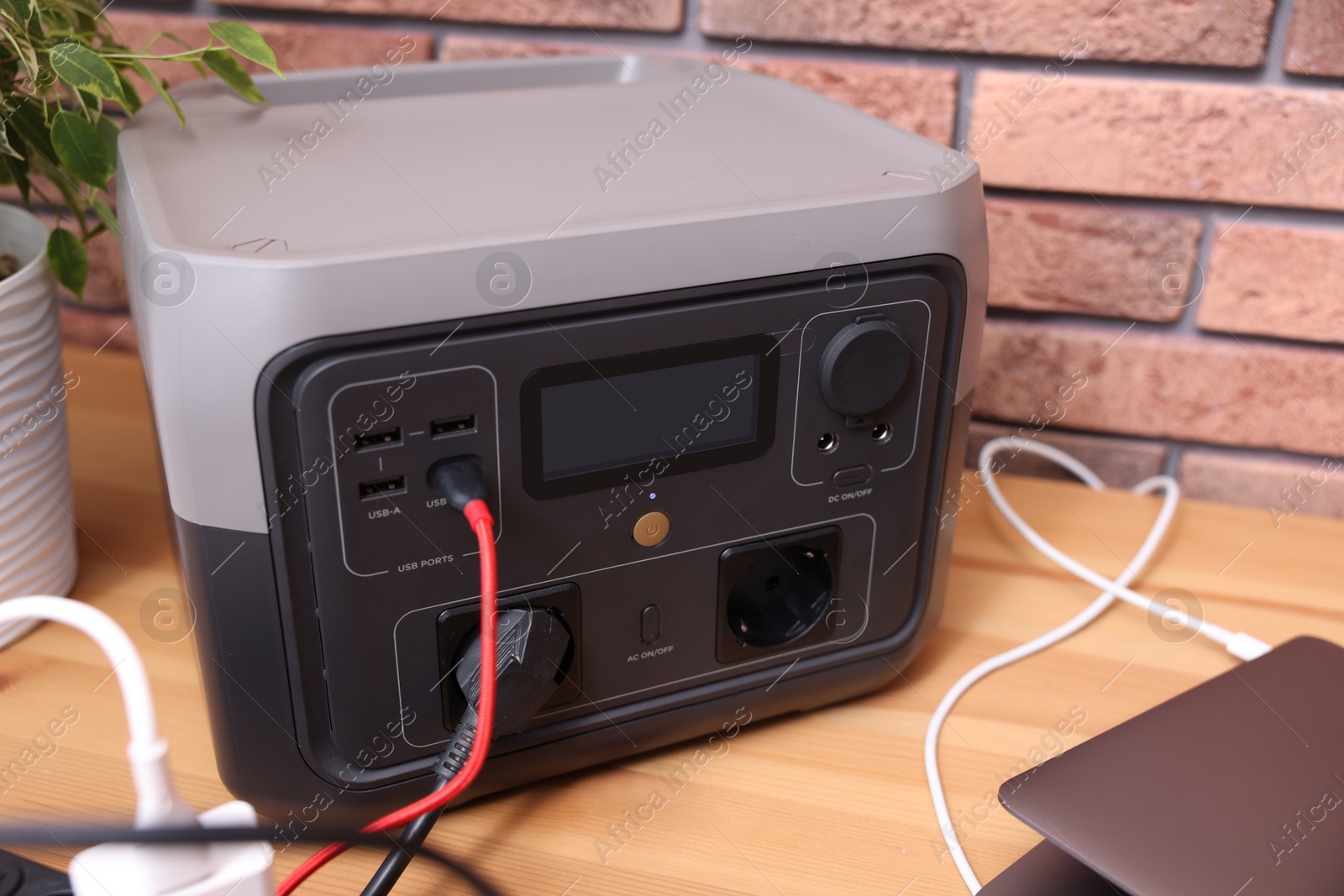 Photo of Laptop charging from portable power station on wooden desk indoors