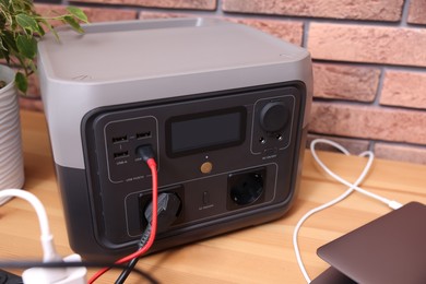 Photo of Laptop charging from portable power station on wooden desk indoors