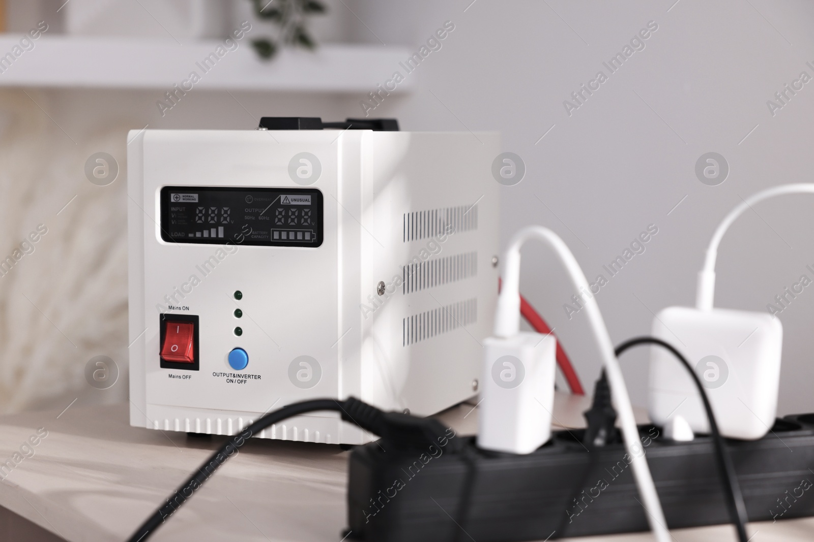 Photo of Portable power station and multi-socket extension board with chargers on table indoors