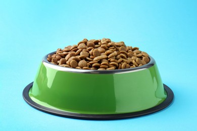 Photo of Dry pet food in feeding bowl on light blue background