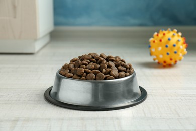 Photo of Dry pet food in feeding bowl and chew bones on floor indoors