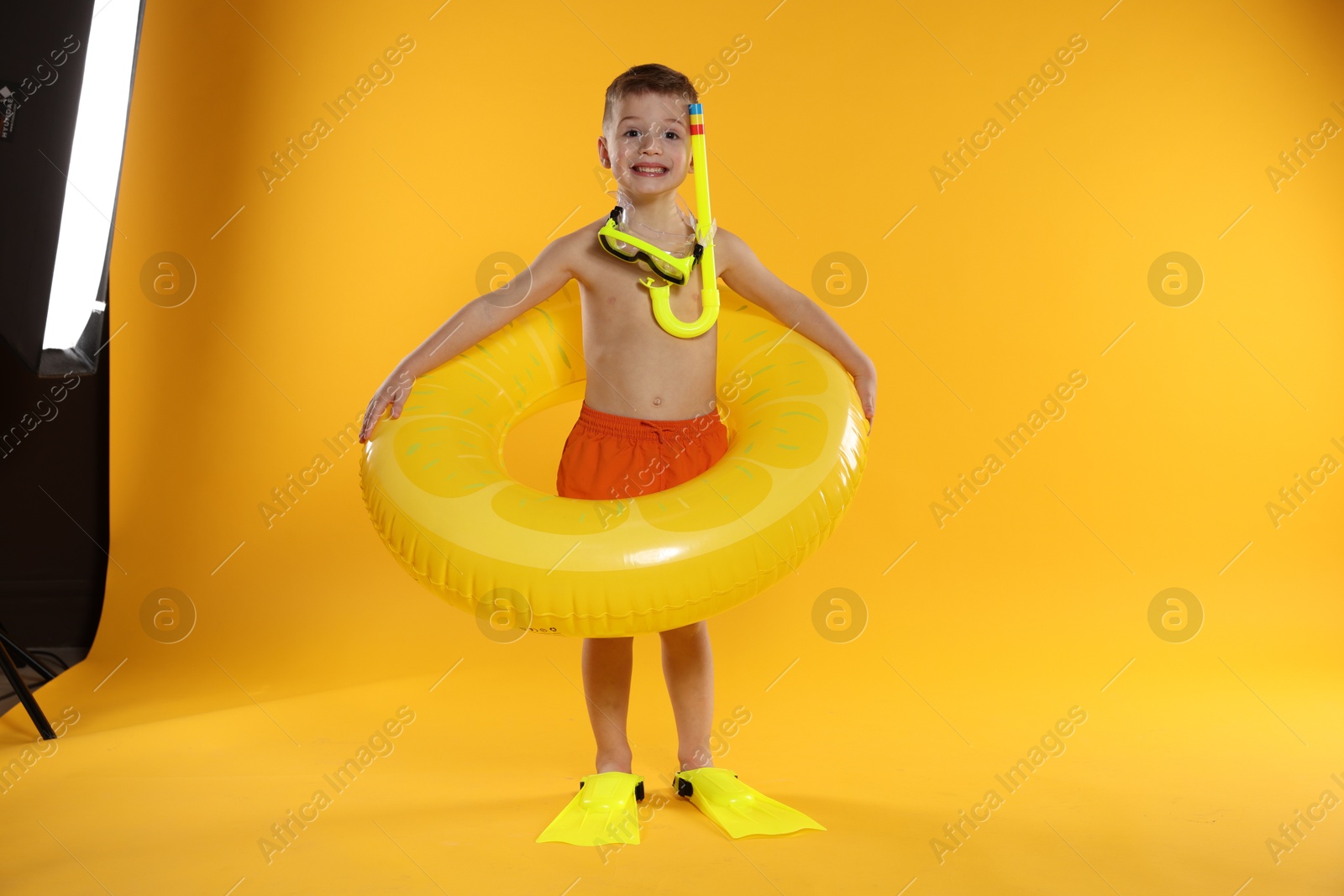 Photo of Cute little boy in beachwear with snorkeling equipment and inflatable ring on orange background