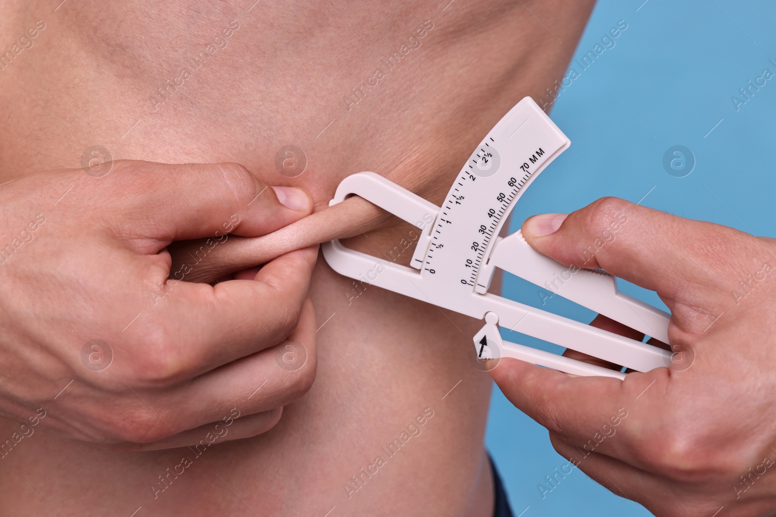 Photo of Man measuring body fat with caliper on light blue background, closeup