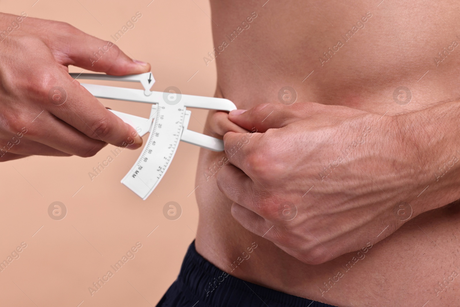 Photo of Man measuring body fat with caliper on beige background, closeup