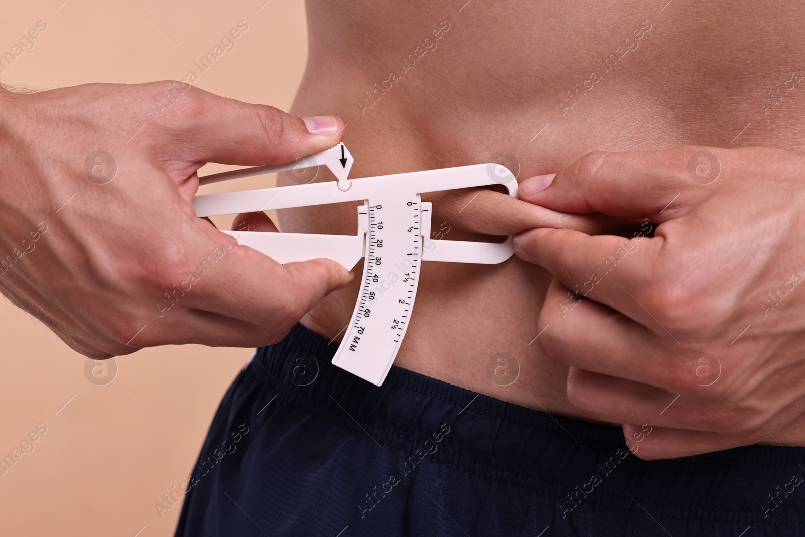 Photo of Man measuring body fat with caliper on beige background, closeup