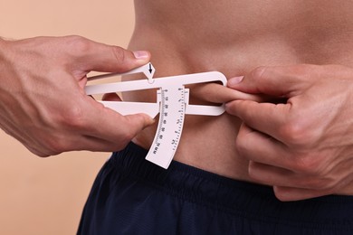 Photo of Man measuring body fat with caliper on beige background, closeup