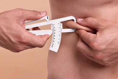 Photo of Man measuring body fat with caliper on beige background, closeup