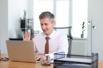 Smiling middle aged man having videochat via laptop at table in office