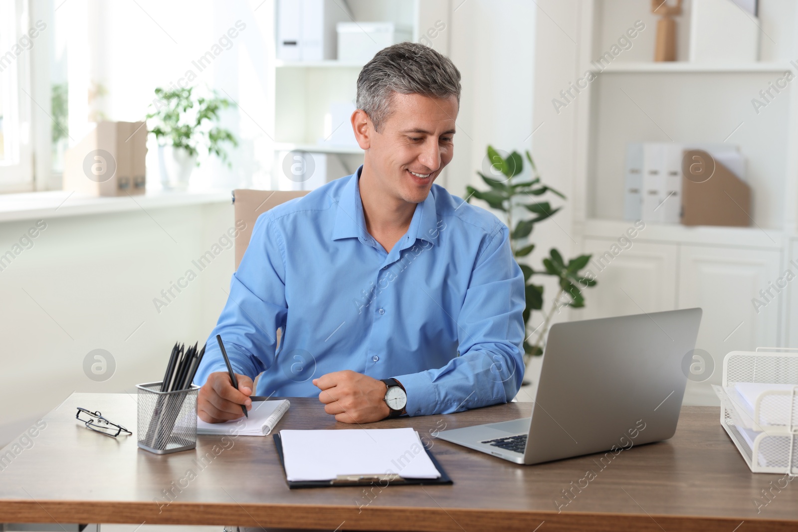 Photo of Smiling middle aged man working with laptop at table in office