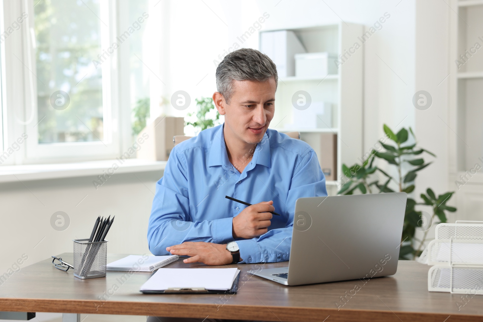 Photo of Middle aged man working with laptop at table in office