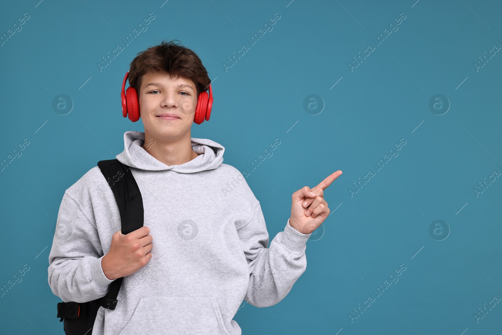 Photo of Teenage boy in headphones with backpack on light blue background, space for text