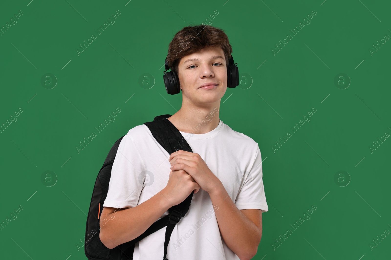 Photo of Teenage boy in headphones with backpack on green background