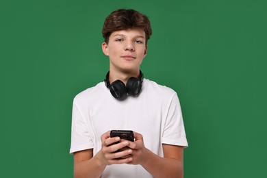 Photo of Teenage boy with headphones and smartphone on green background