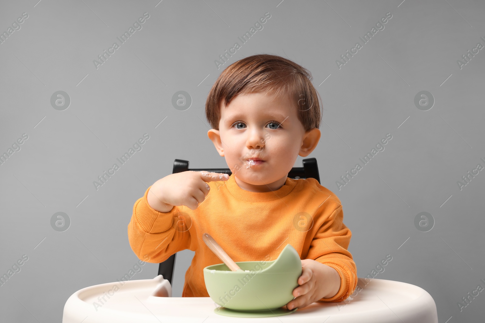 Photo of Cute little kid eating healthy baby food from bowl in high chair on light grey background