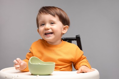 Photo of Cute little kid eating healthy baby food from bowl in high chair on light grey background