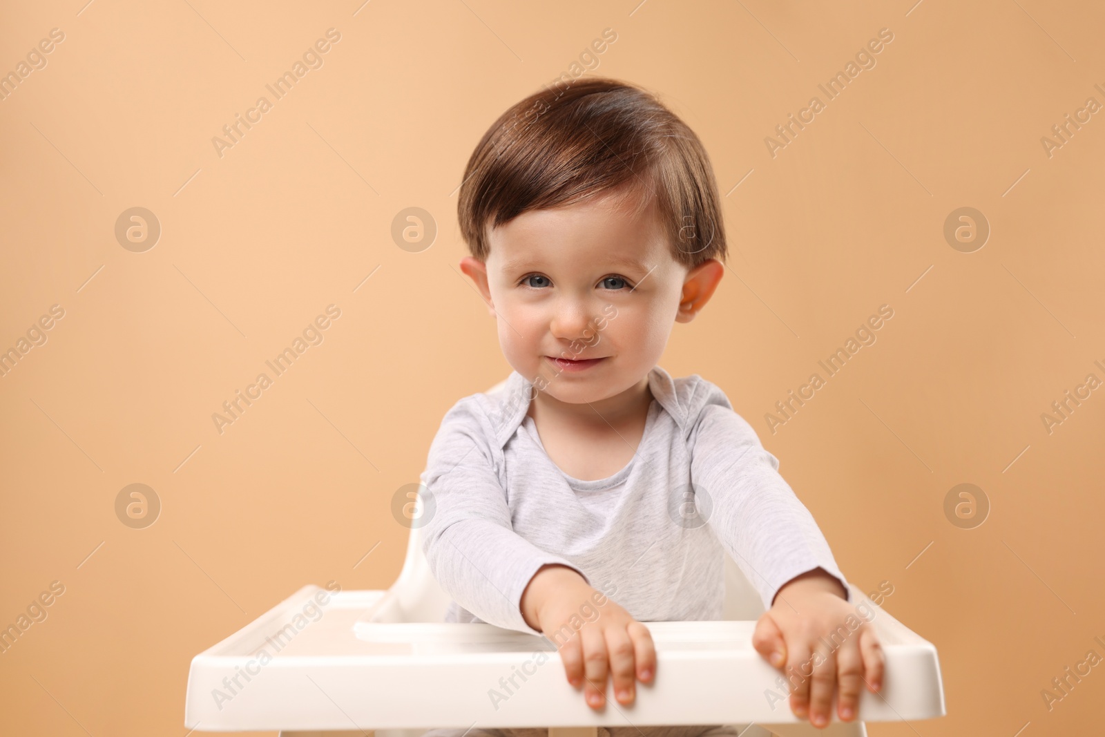 Photo of Cute little kid sitting in high chair on beige background