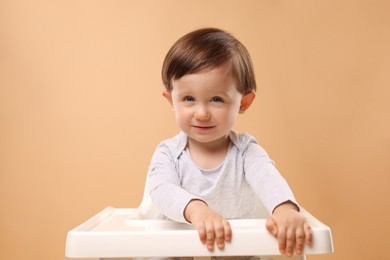 Photo of Cute little kid sitting in high chair on beige background