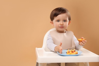 Photo of Healthy baby food. Cute little kid eating fruits in high chair on beige background