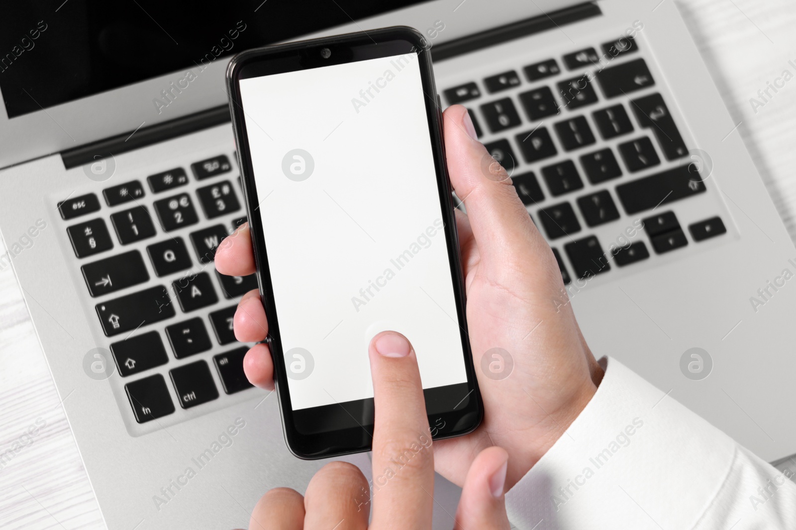 Photo of Man unlocking smartphone with fingerprint scanner near laptop at light wooden table, closeup