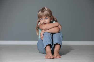 Photo of Orphanage concept. Sad little girl sitting on floor near grey wall