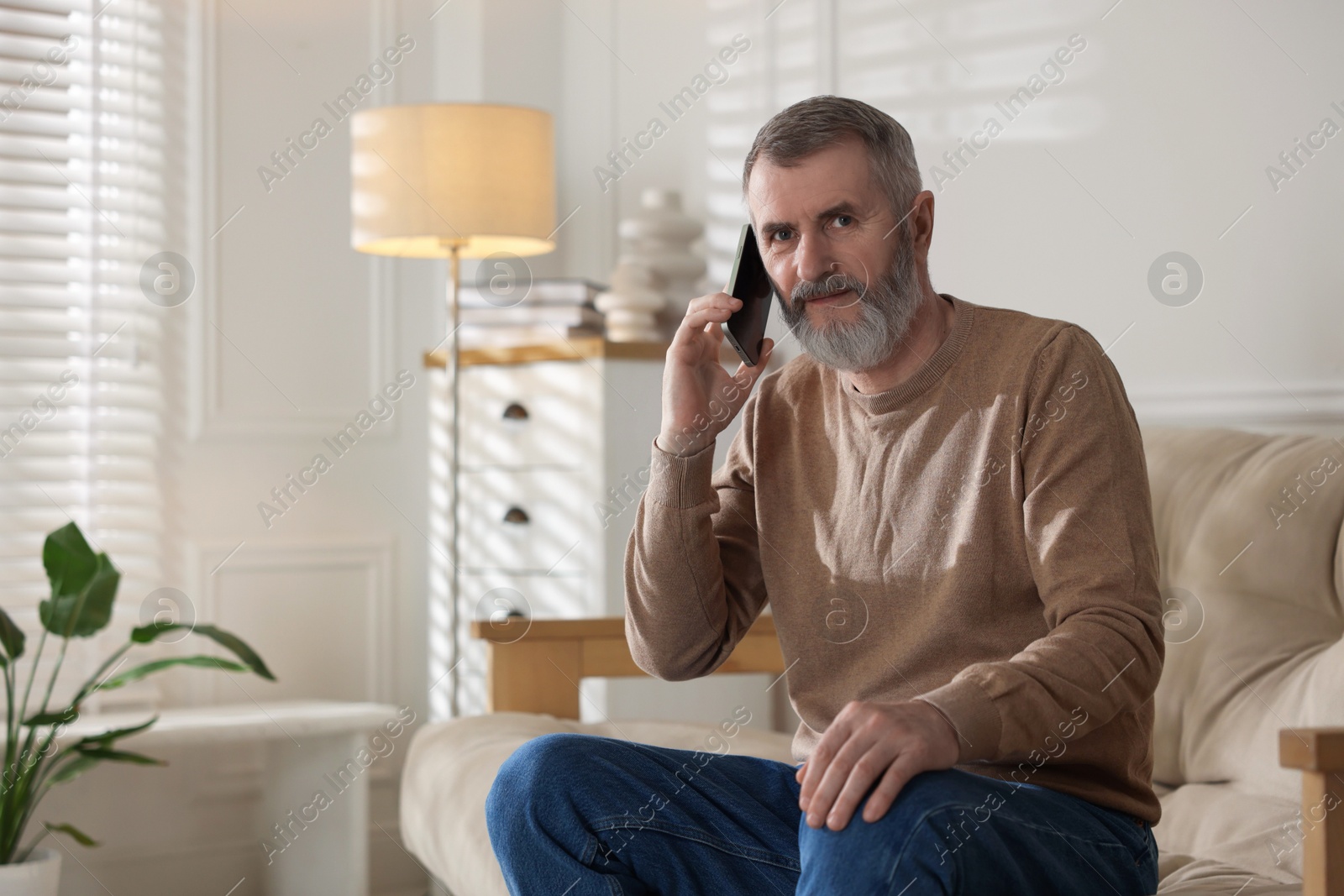 Photo of Senior man talking on smartphone at home