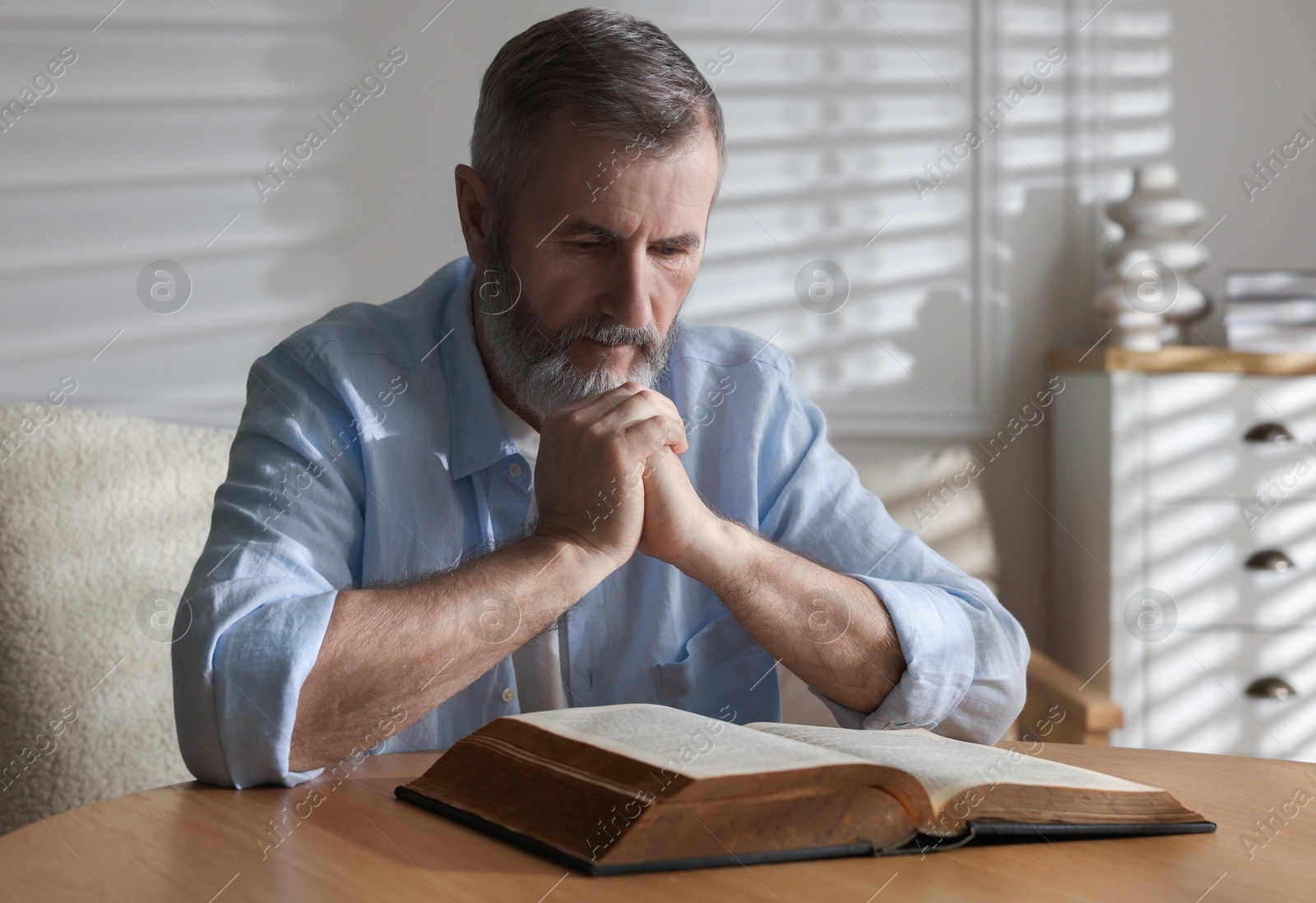 Photo of Senior man reading book at table indoors