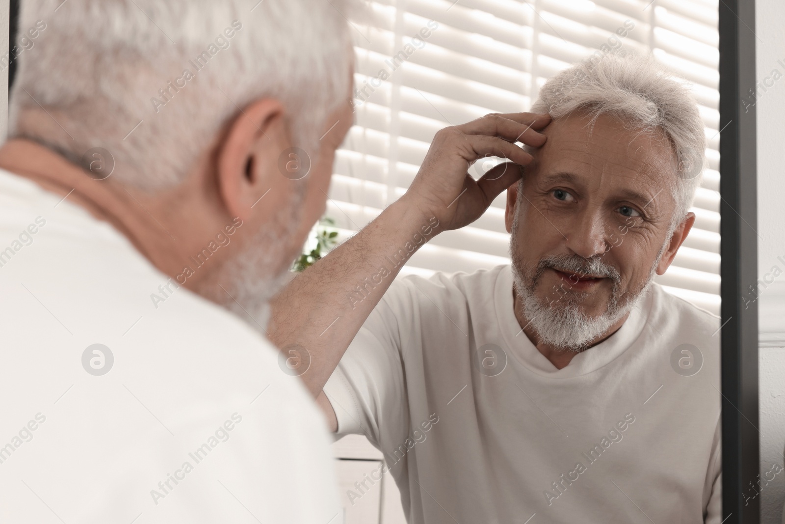 Photo of Senior man looking in mirror at home