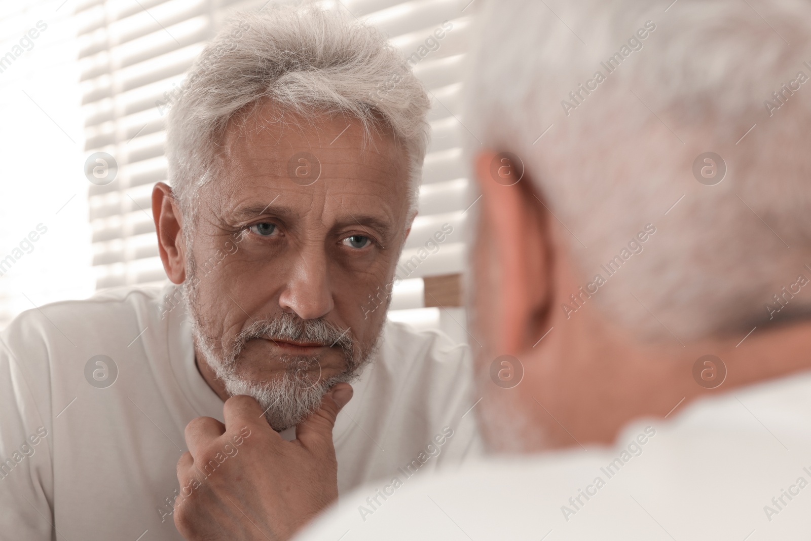 Photo of Senior man looking in mirror at home