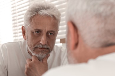 Photo of Senior man looking in mirror at home