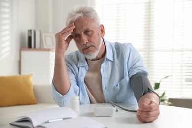 Photo of Senior man measuring blood pressure at table indoors