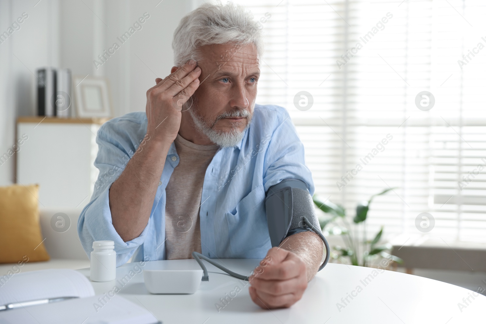 Photo of Senior man measuring blood pressure at table indoors