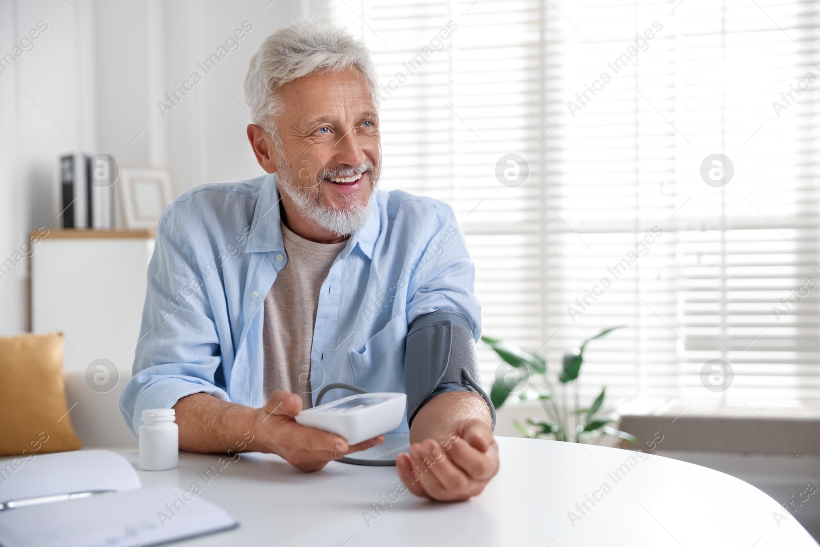 Photo of Senior man measuring blood pressure at table indoors