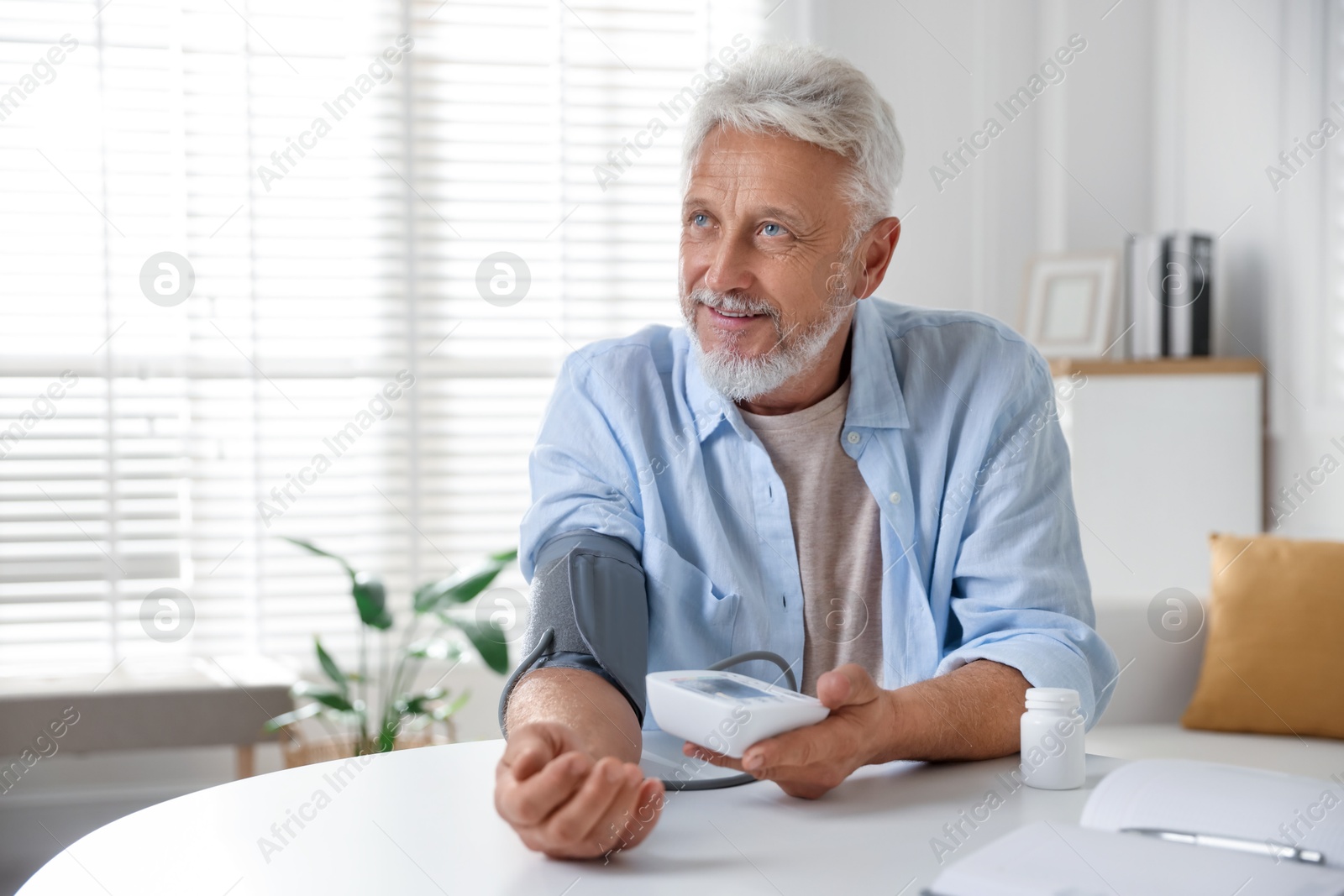 Photo of Senior man measuring blood pressure at table indoors