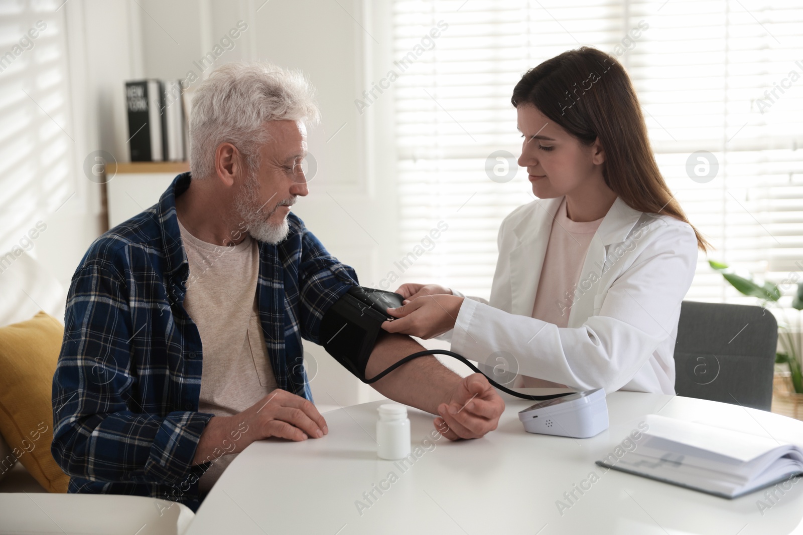 Photo of Doctor measuring patient's blood pressure at table in hospital