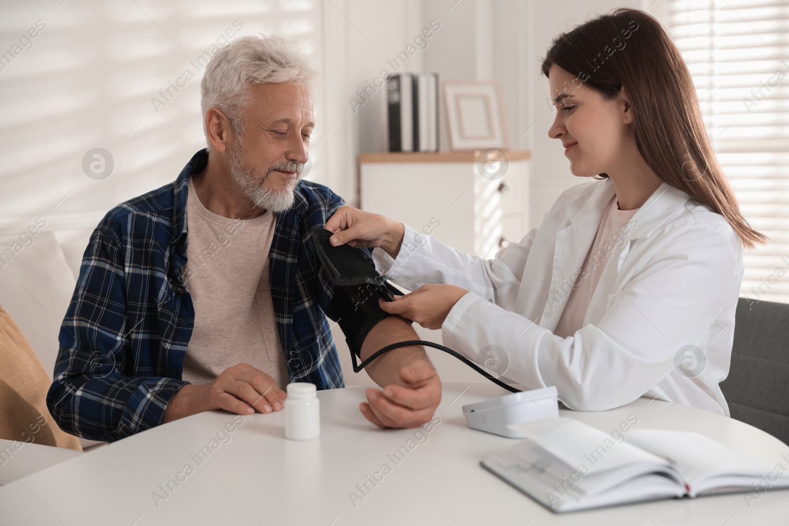 Photo of Doctor measuring patient's blood pressure at table in hospital