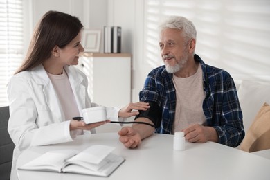 Photo of Doctor measuring patient's blood pressure at table in hospital