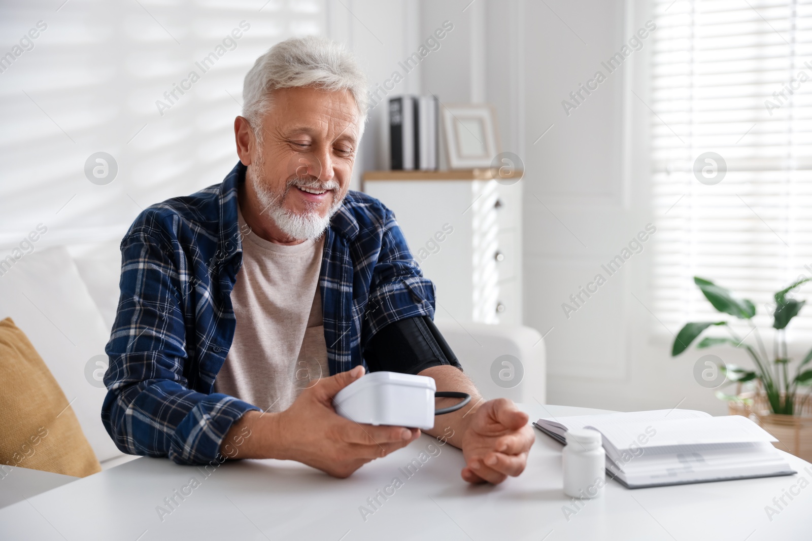 Photo of Senior man measuring blood pressure at table indoors